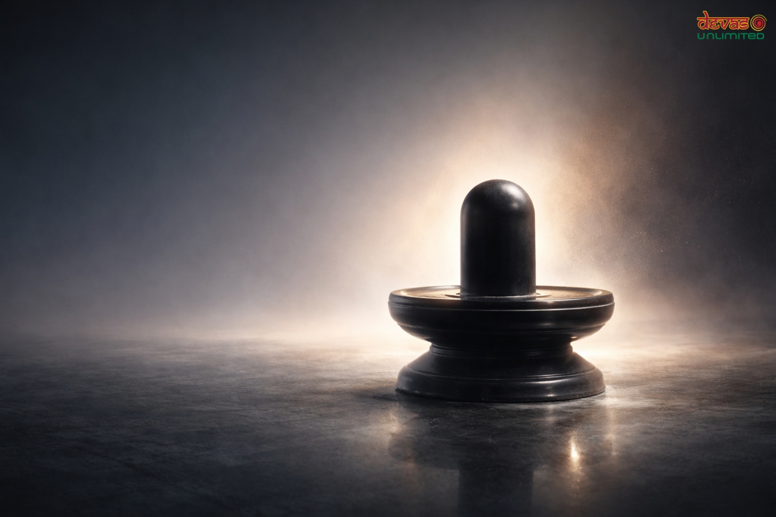 Black Shivlingam illuminated by a soft golden light against a dark background.